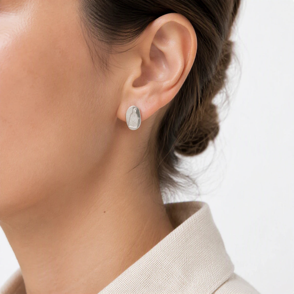 Sterling silver earring featuring a bottle motif worn on the left ear, shown in a close-up contemporary jewellery portrait against a soft white background, from the At the Table with Morandi collection by Inês Almeida.