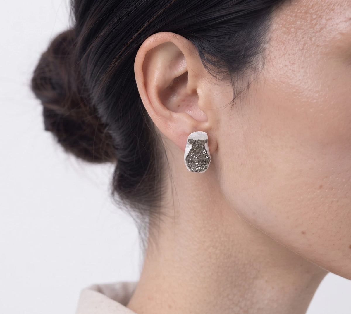 Sterling silver earring featuring a jug motif worn on the ear, shown in a close-up contemporary jewellery portrait against a soft white background, by Inês Almeida.