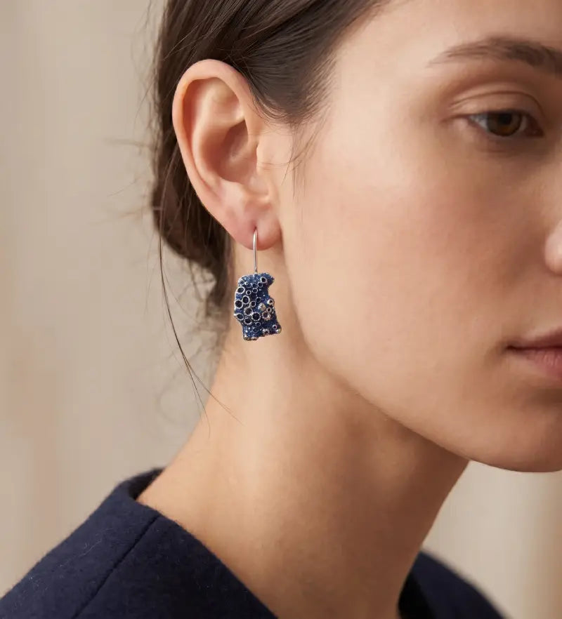 A female model wearing 925 sterling silver earrings barnacle painted with blue. Design by Inês Almeida.