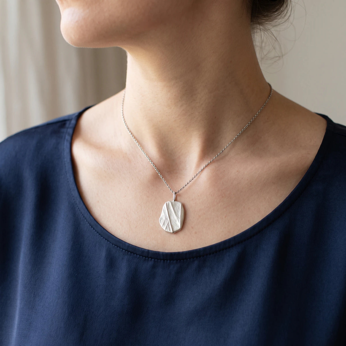Woman wearing 925 sterling silver pendant with the texture from a pebble. Design by Inês Almeida