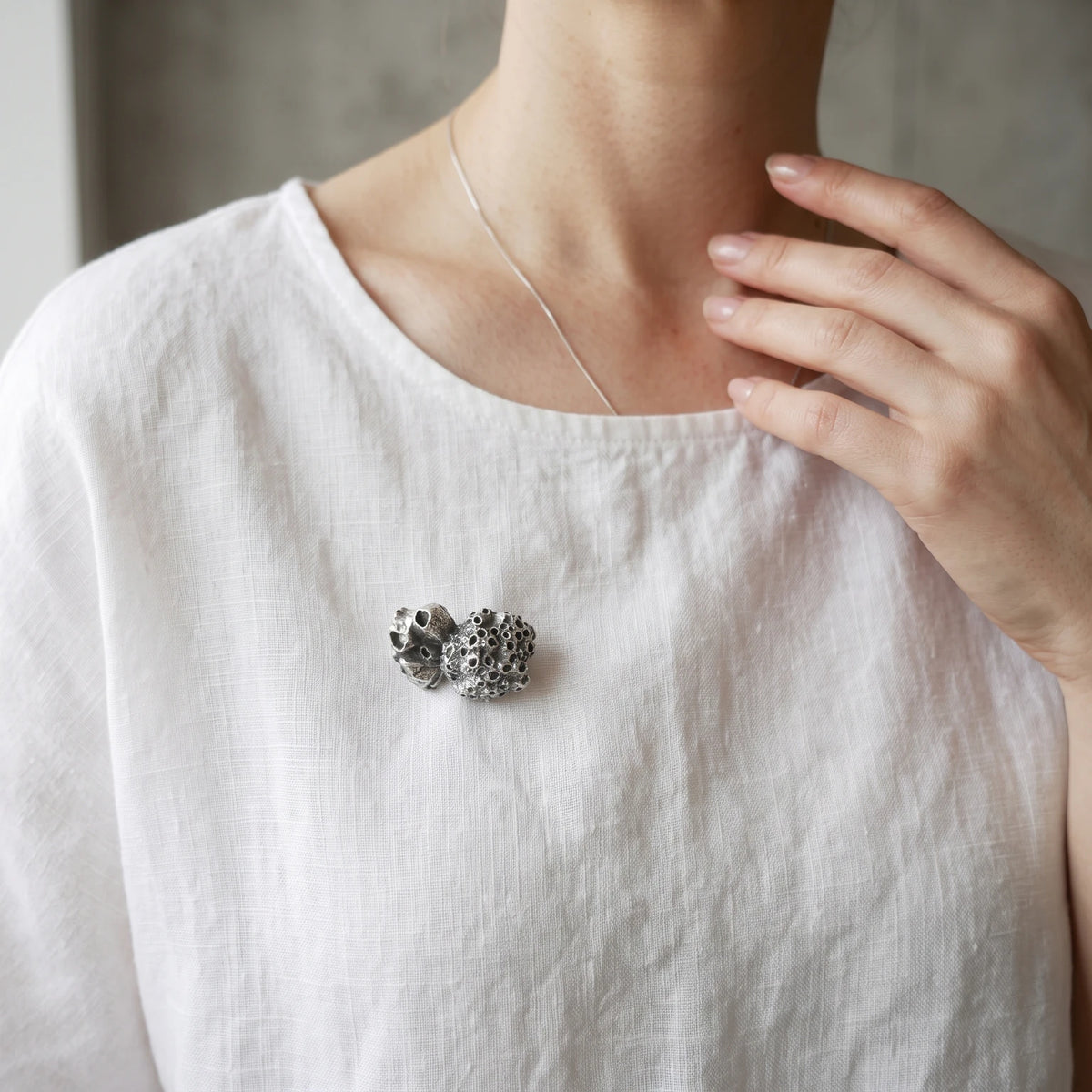 Woman wearing a 925 sterling oxidised silver brooch with the texture from a barnacle. Design by Inês Almeida