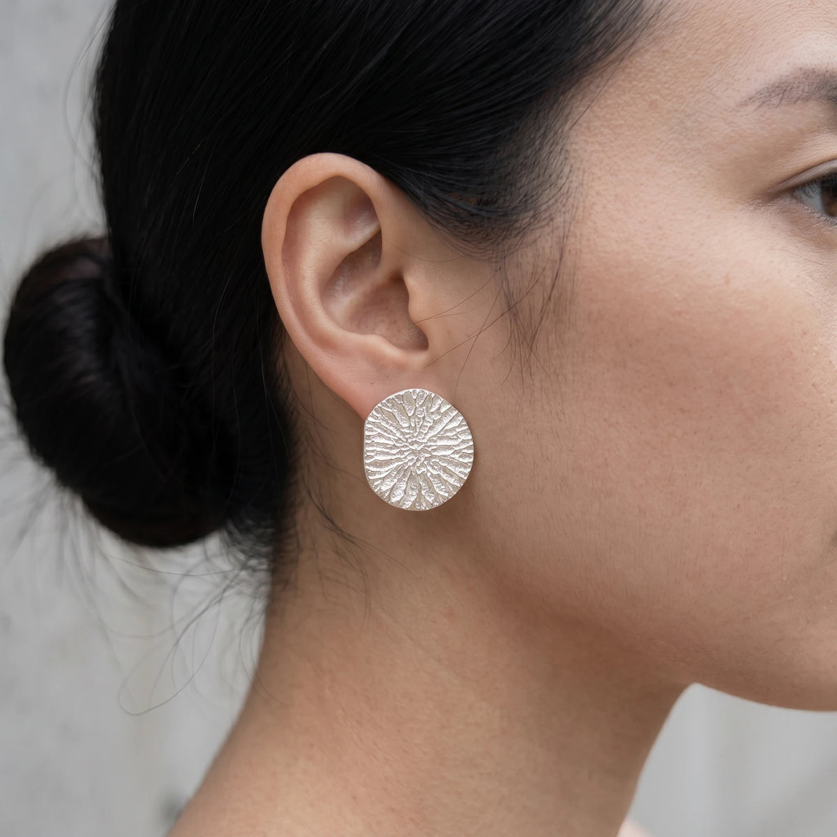 A female model wearing 925 sterling silver earrings with the texture from a dolphin spine bone. Design by Inês Almeida.