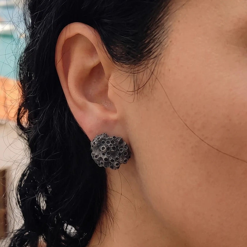 A female model wearing 925 sterling oxidized silver barnacle earrings by Inês Almeida on a beach setting.