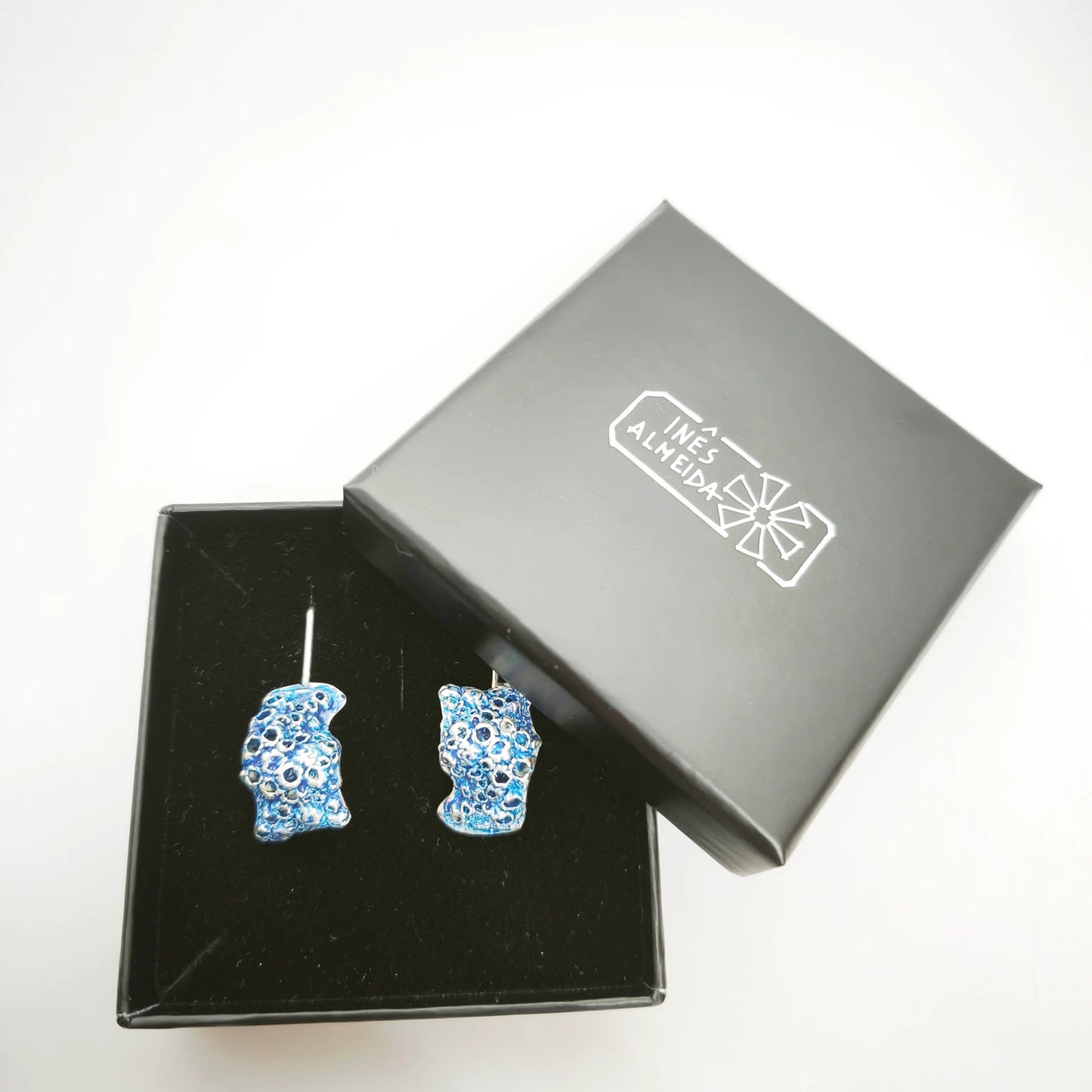 925 sterling silver earrings with the texture from a barnacle painted with blue in a jewellery box. Design by Inês Almeida