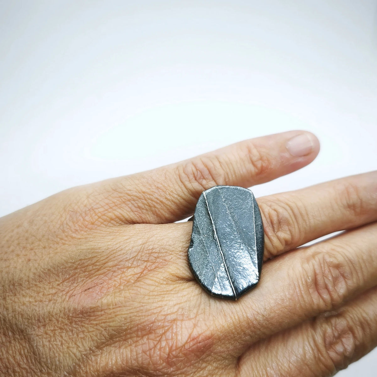 Woman wearing a 925 sterling silver oxidised ring with the texture from small pebble. Design by Inês Almeida