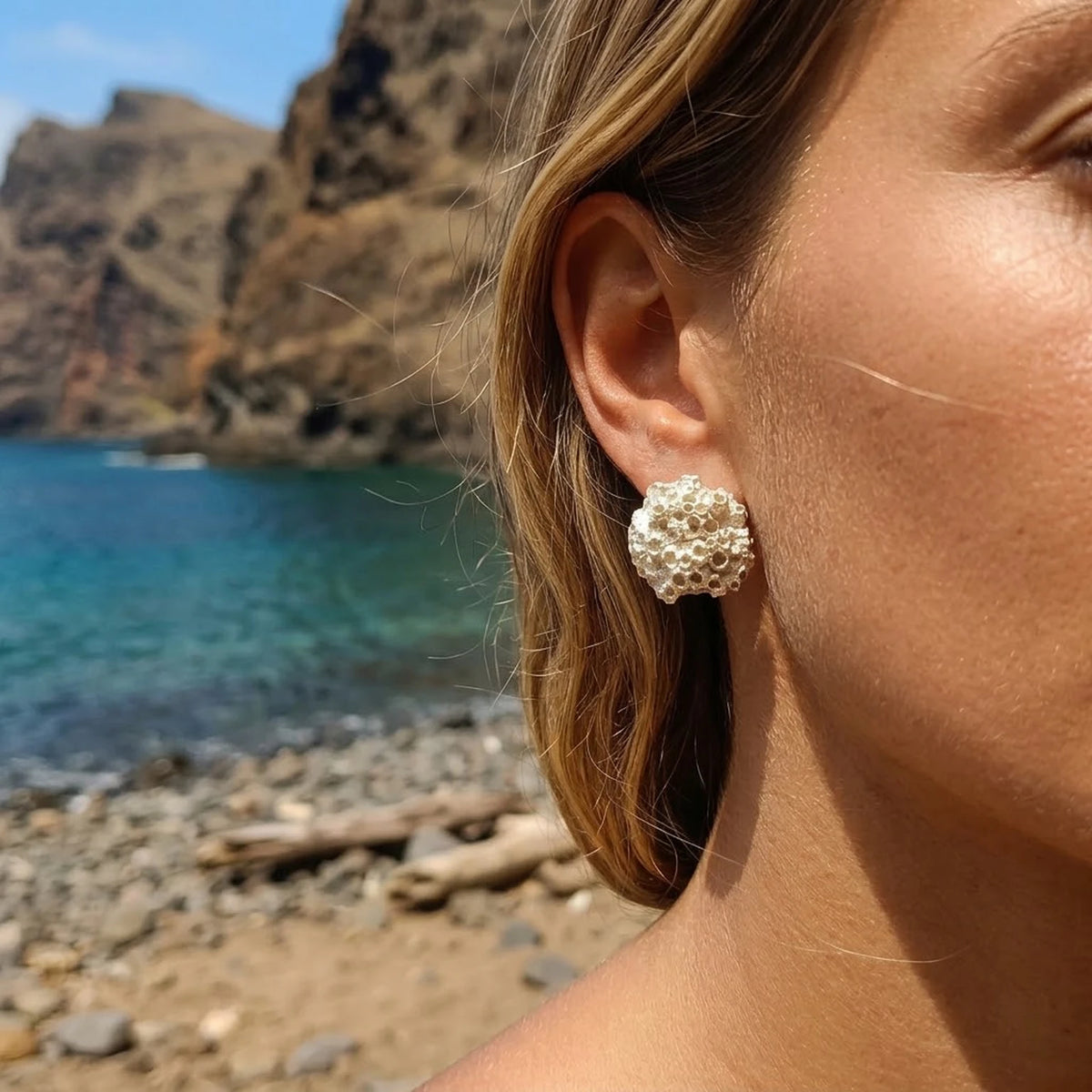 A female model wearing 925 sterling silver barnacle earrings by Inês Almeida on a beach setting.