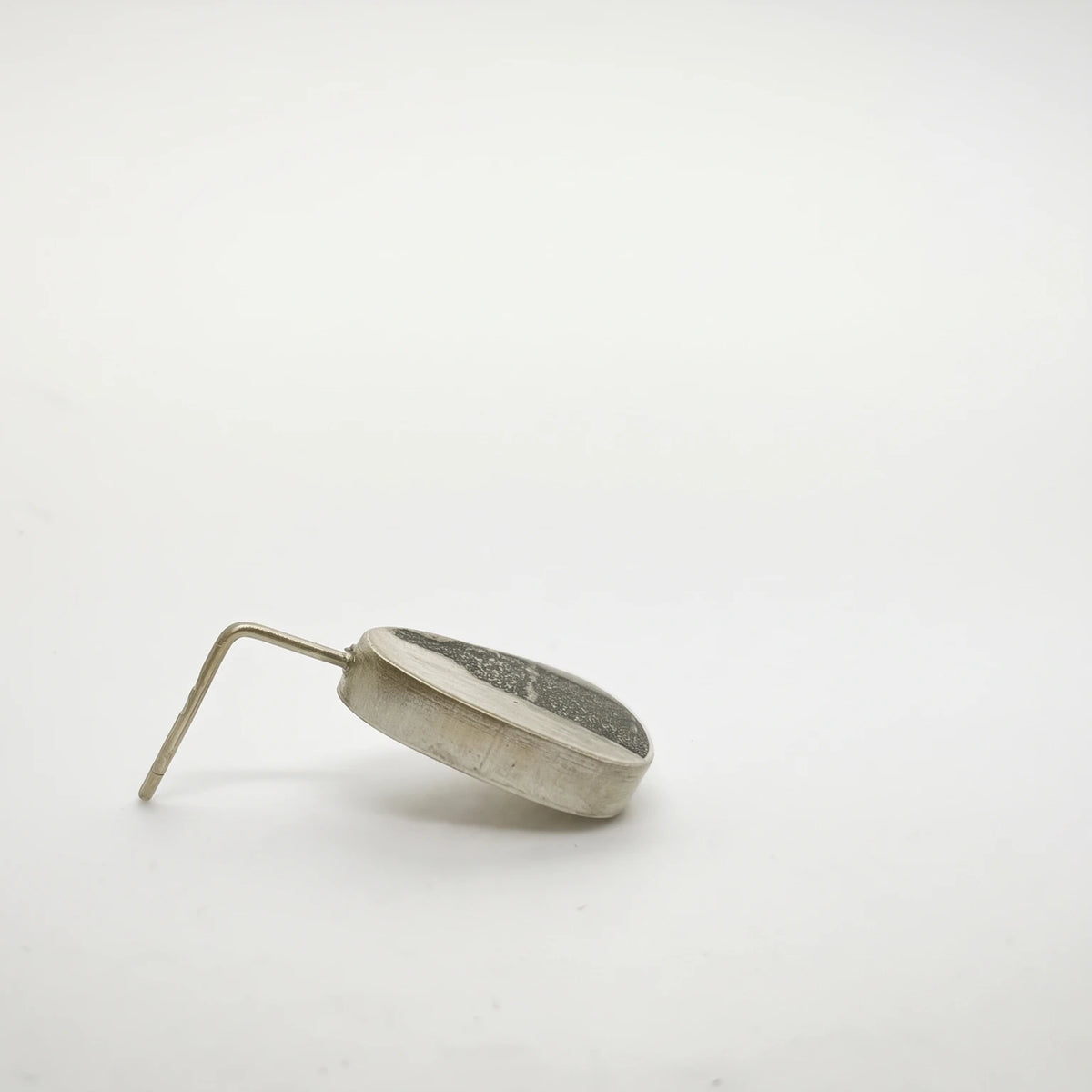 Profile view of a sterling silver drop earring featuring a black bottle motif, showing its depth and hook fastening, by Inês Almeida.