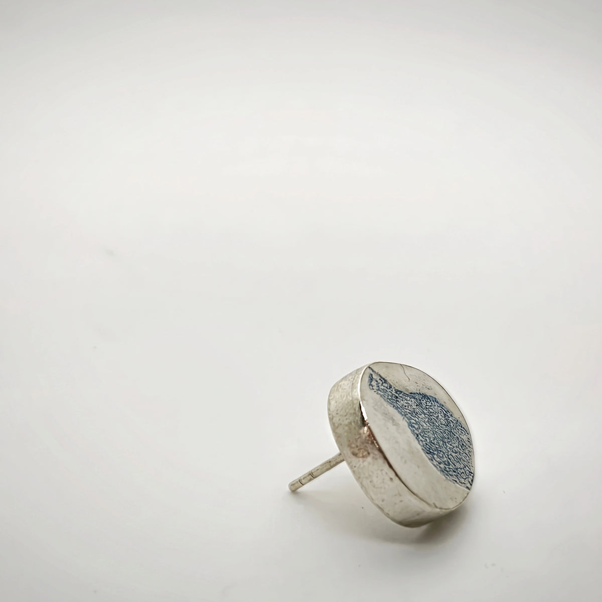 Profile view of a sterling silver earring featuring a blue bottle motif, showing its depth and post fastening, by Inês Almeida.
