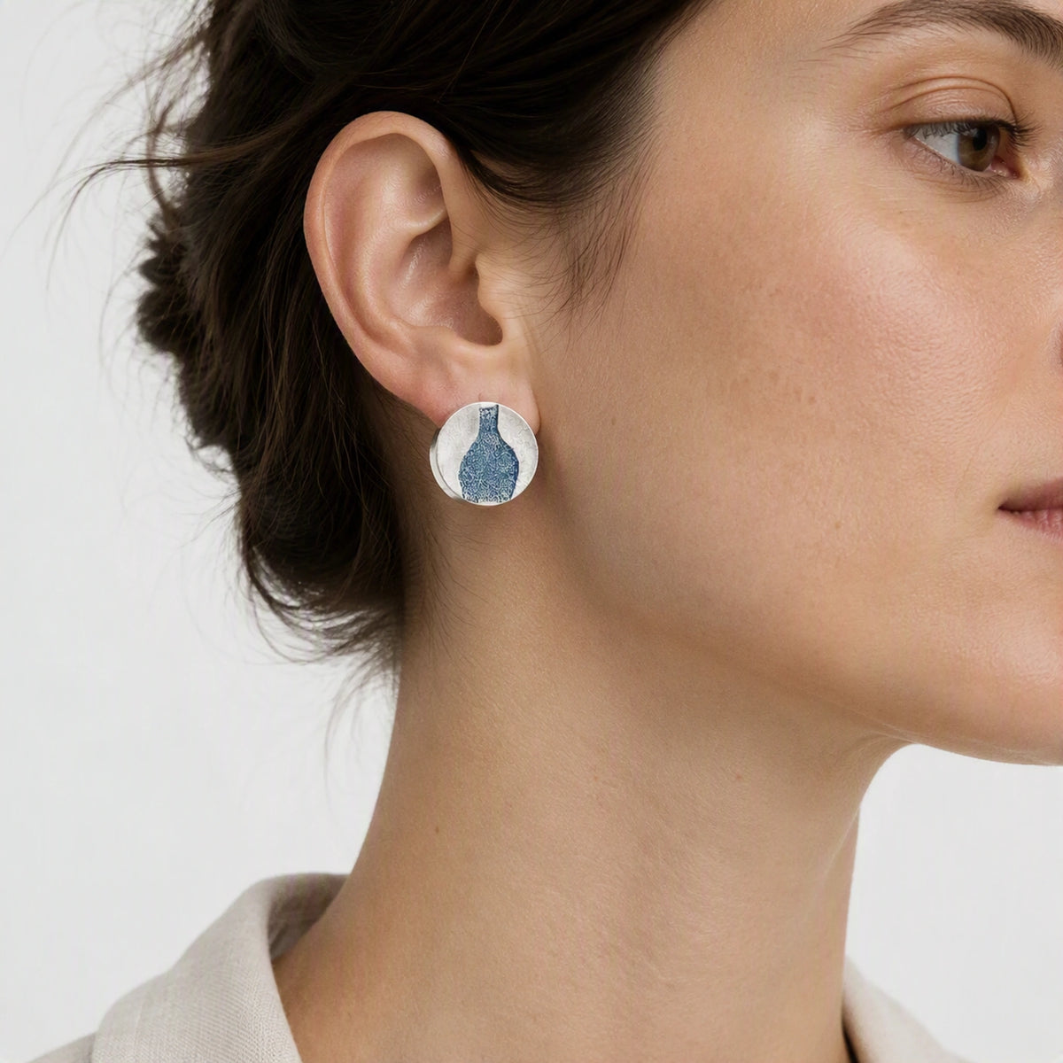 Sterling silver earring featuring a blue bottle motif worn on one ear, with the head slightly turned towards the camera against a soft white background, from the At the Table with Morandi collection by Inês Almeida.