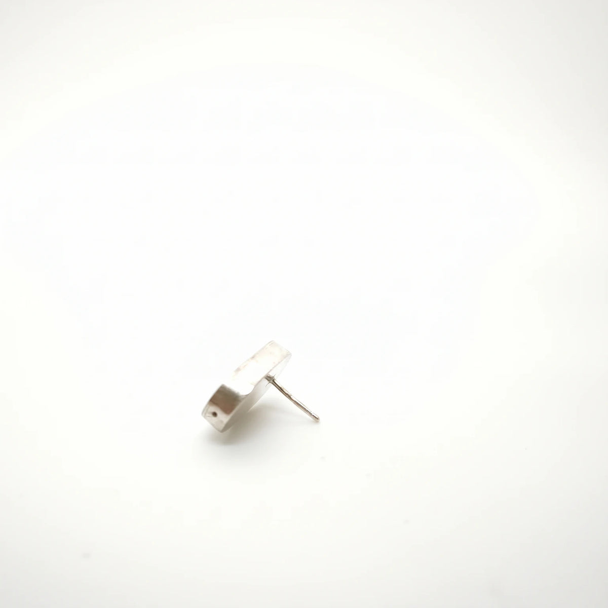 Profile view of a sterling silver earring featuring a bottle motif, showing its depth and post fastening, by Inês Almeida.
