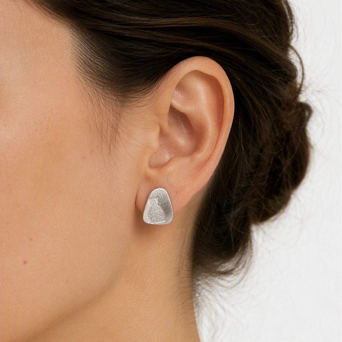 Sterling silver earring featuring a bottle motif worn on the left ear, with the head slightly turned towards the camera against a soft white background, from the At the Table with Morandi collection by Inês Almeida.