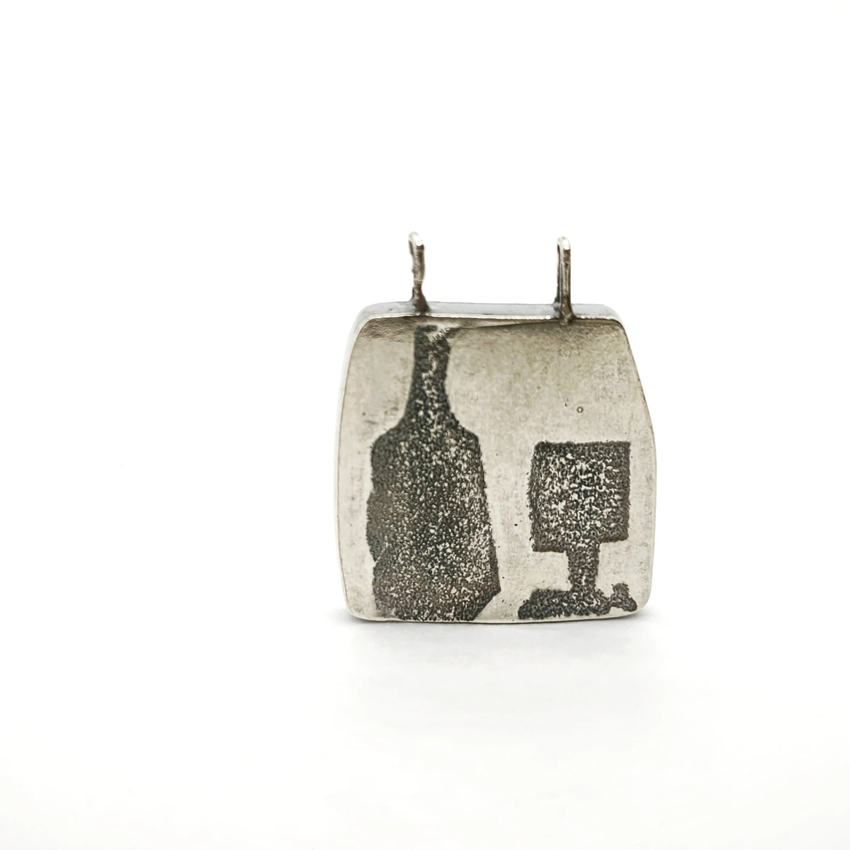 Close-up detail of a sterling silver pendant featuring a bottle and glass motif suspended from a silver chain, by Inês Almeida.