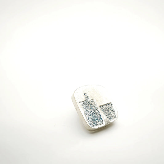Angled view of a sterling silver pin featuring a blue bottle and glass motif.