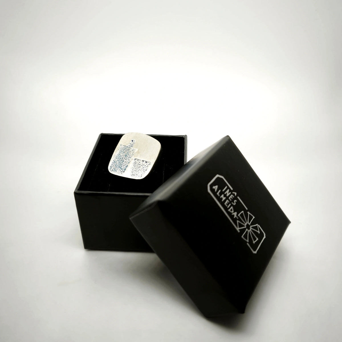 Sterling silver pin featuring a blue bottle and glass motif presented in a black jewellery box by Inês Almeida.