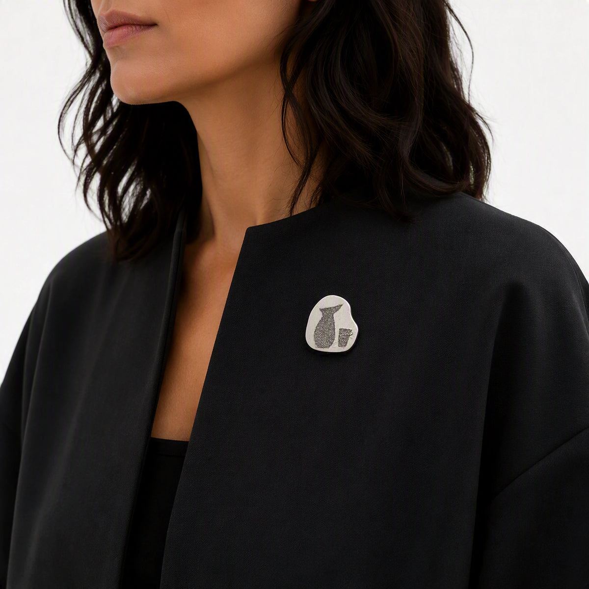 Sterling silver pin with a jug and glass motif worn on a contemporary dark garment, from the At the Table with Morandi collection.
