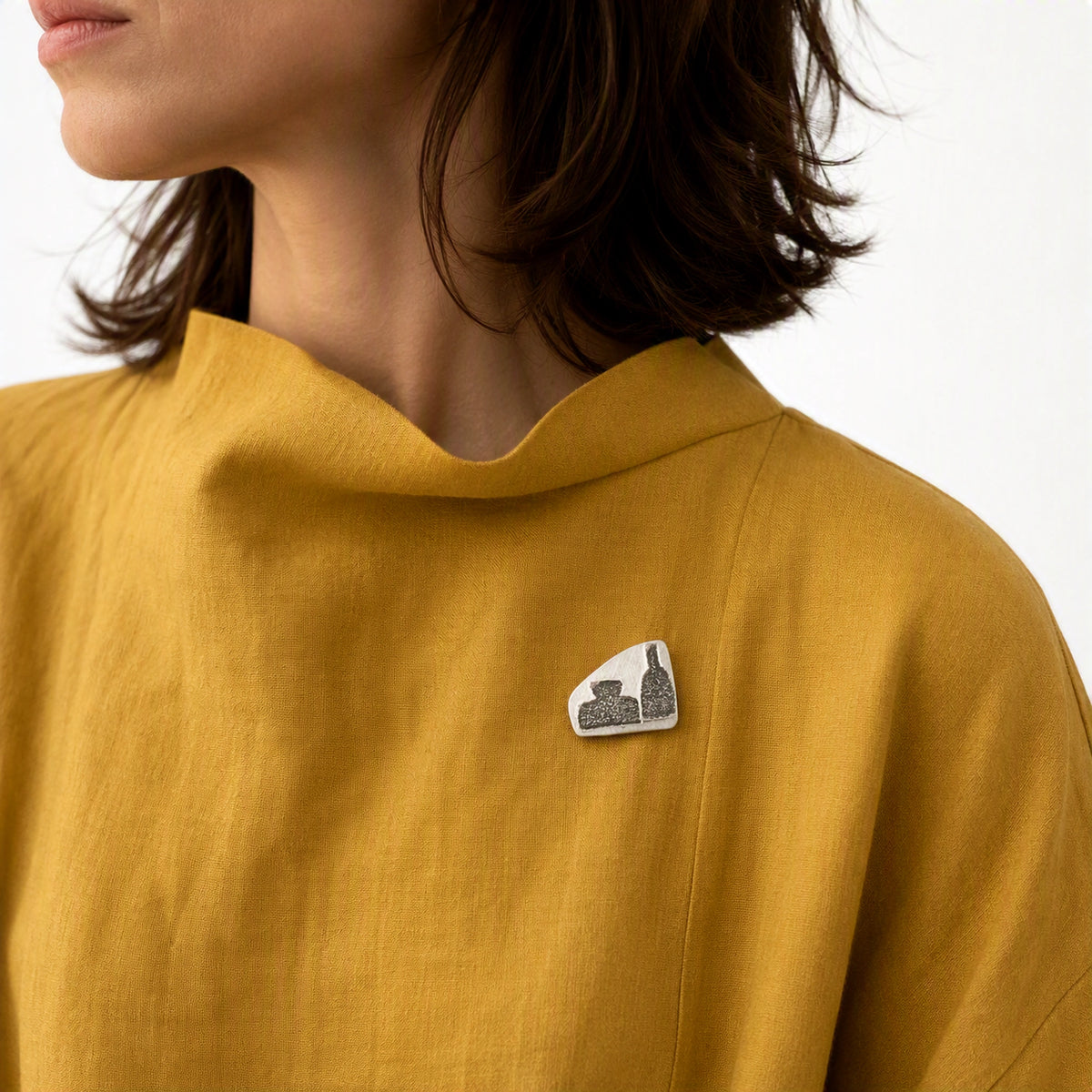 Sterling silver pin featuring two bottle motifs worn on a mustard yellow contemporary garment, from the At the Table with Morandi collection.