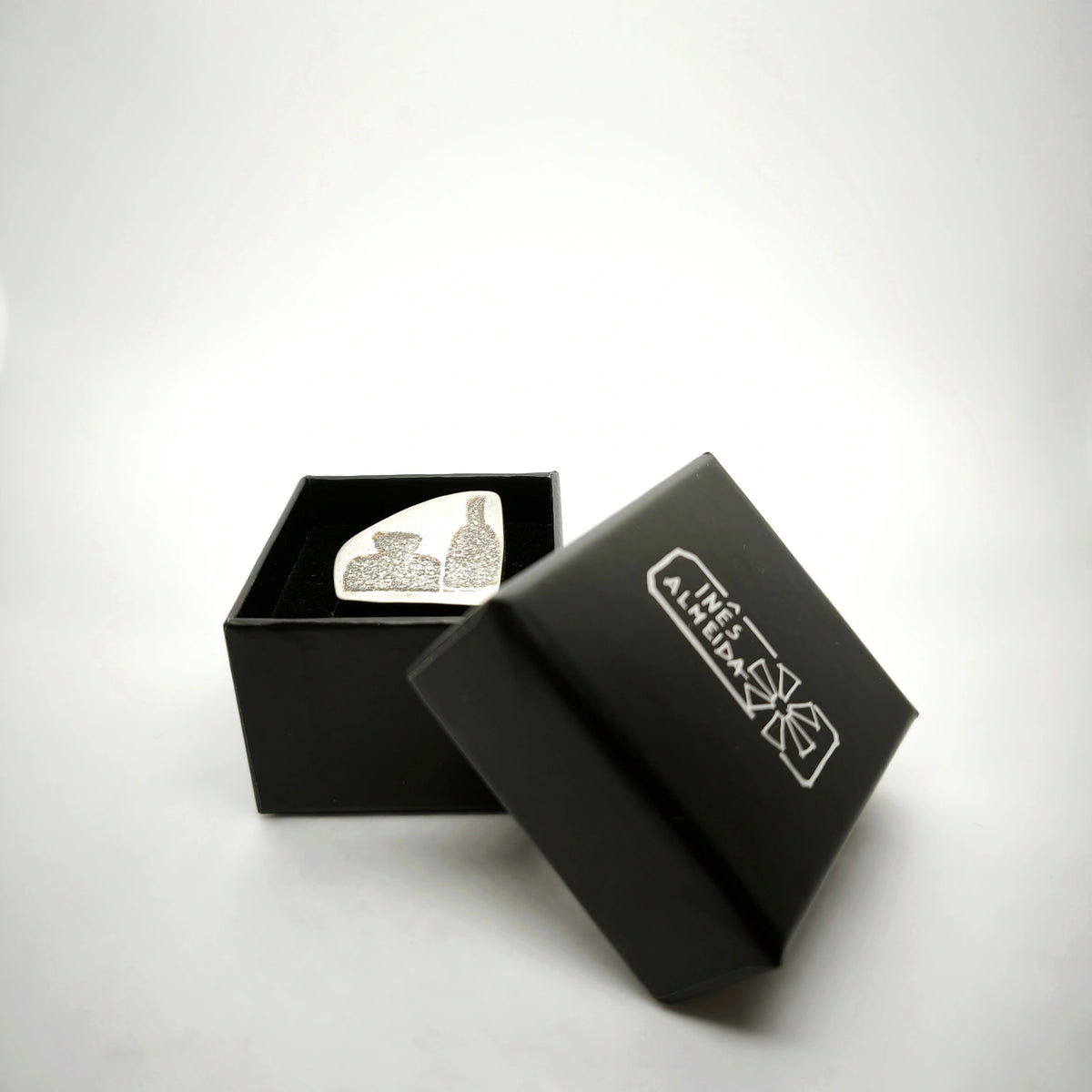Sterling silver pin featuring two bottle motifs displayed in an open black jewellery box by Inês Almeida.