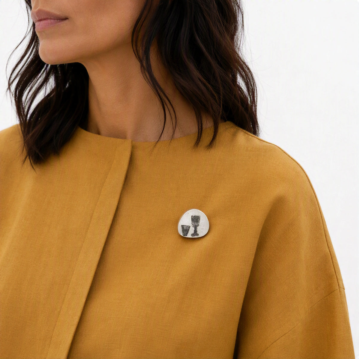 Sterling silver pin featuring two glass motifs worn on a mustard yellow contemporary garment, from the At the Table with Morandi collection.